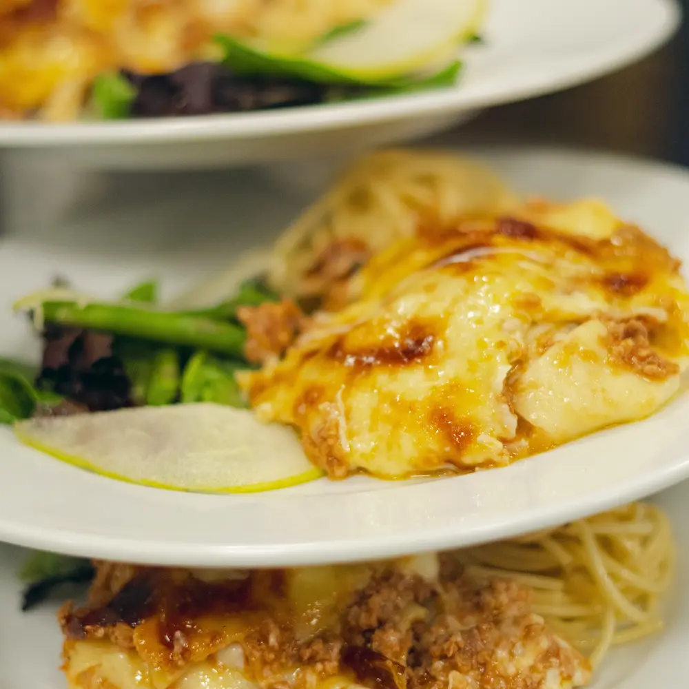 Platos de comida, pasta gratinada con salsa de carne y queso derretido, y verduras.