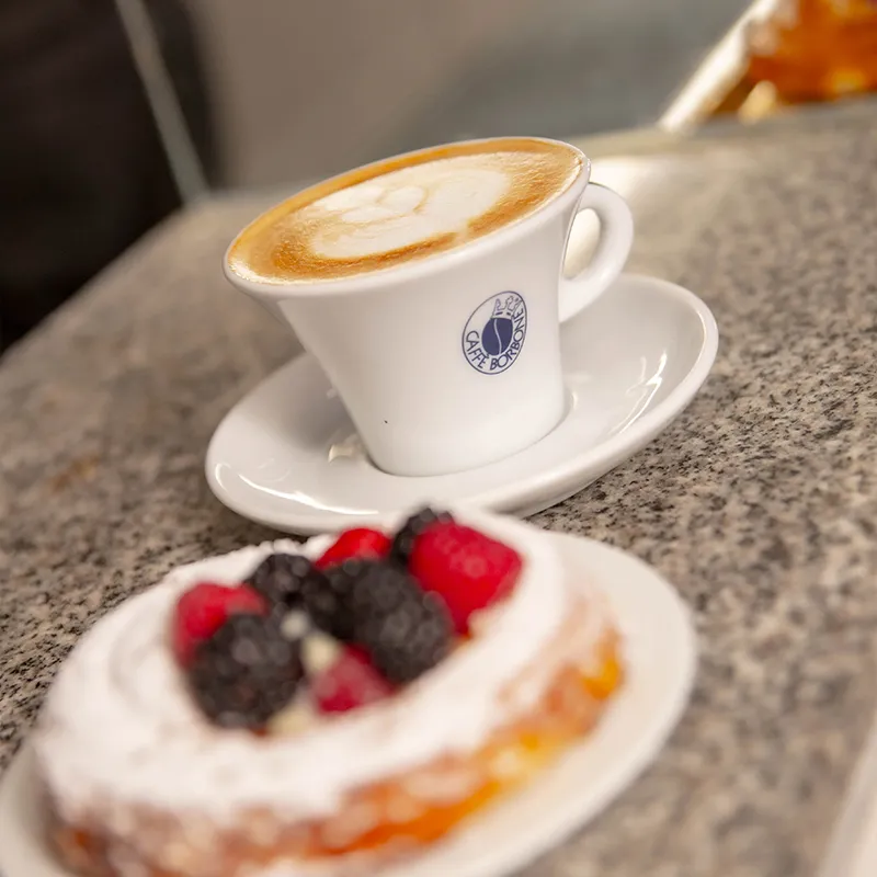 Postre con frutos rojos acompañado de café con arte latte.