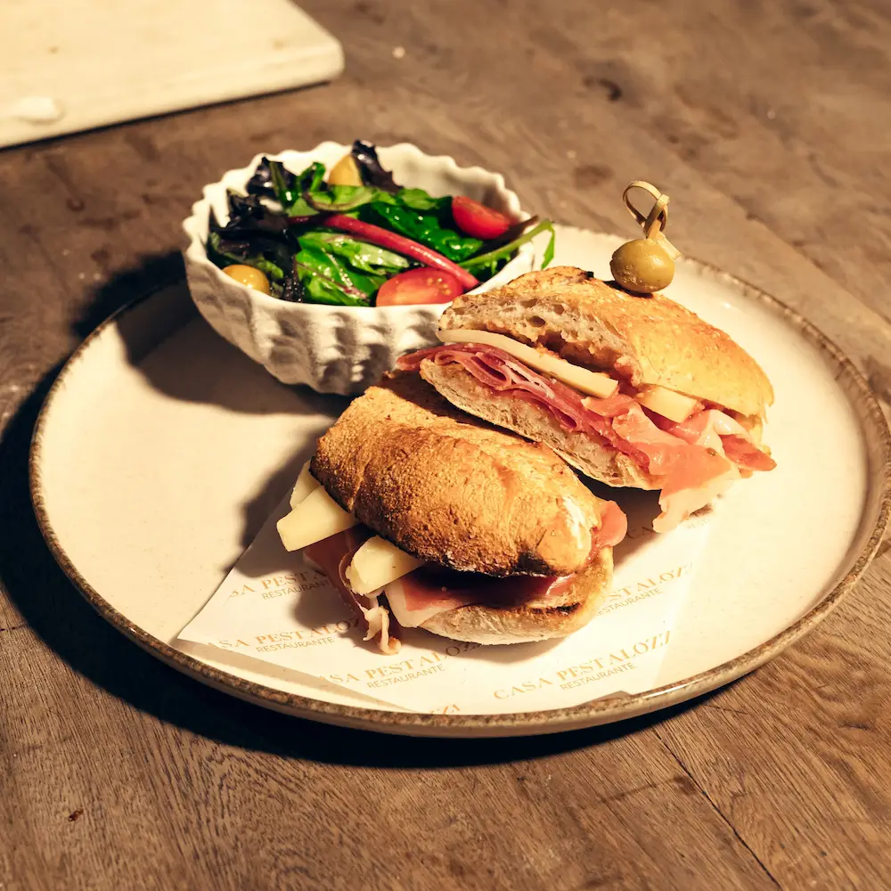 Bocadillo de jamón serrano con queso acompañado con ensalada.