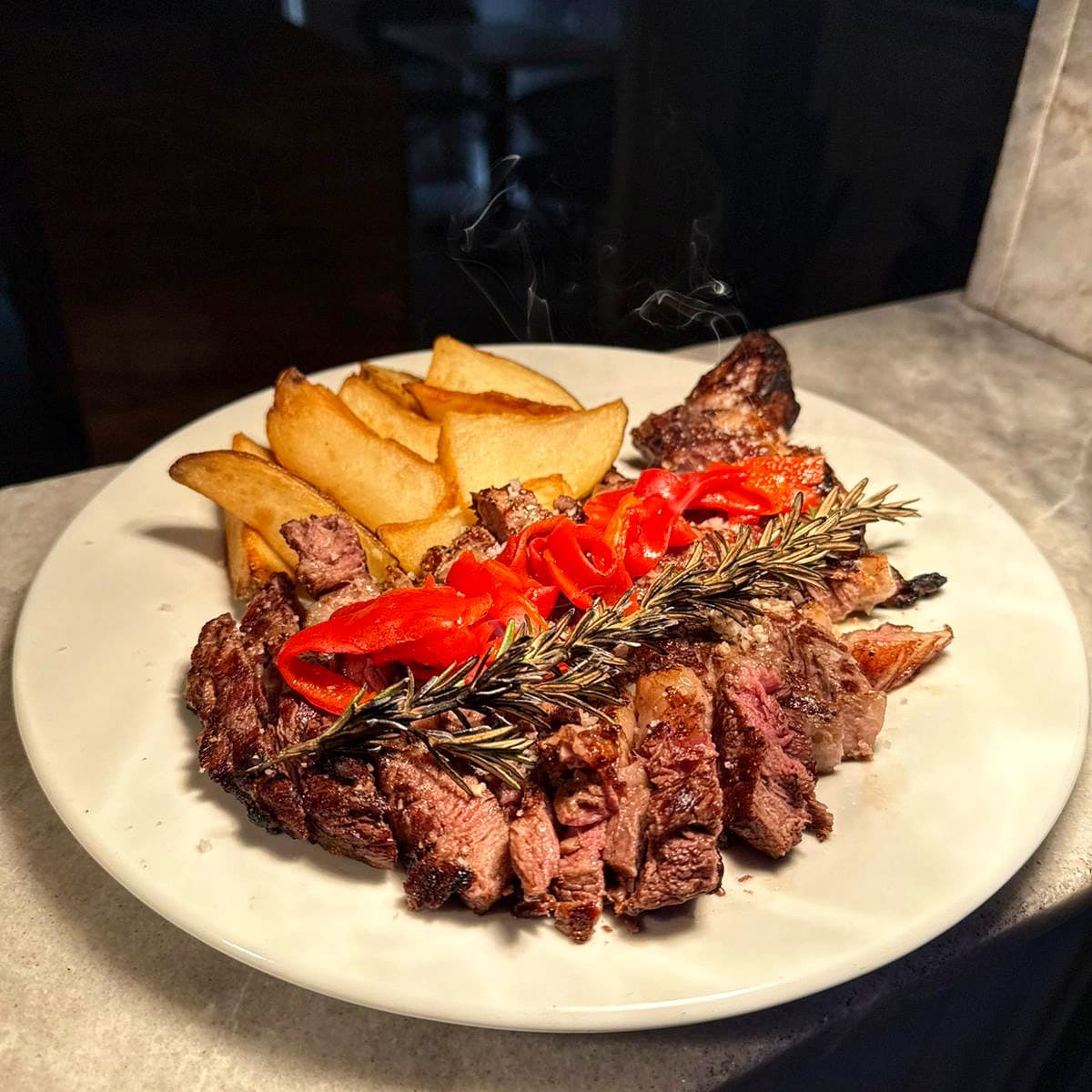 Filete de carne con papas fritas, jitomates asados y romero.
