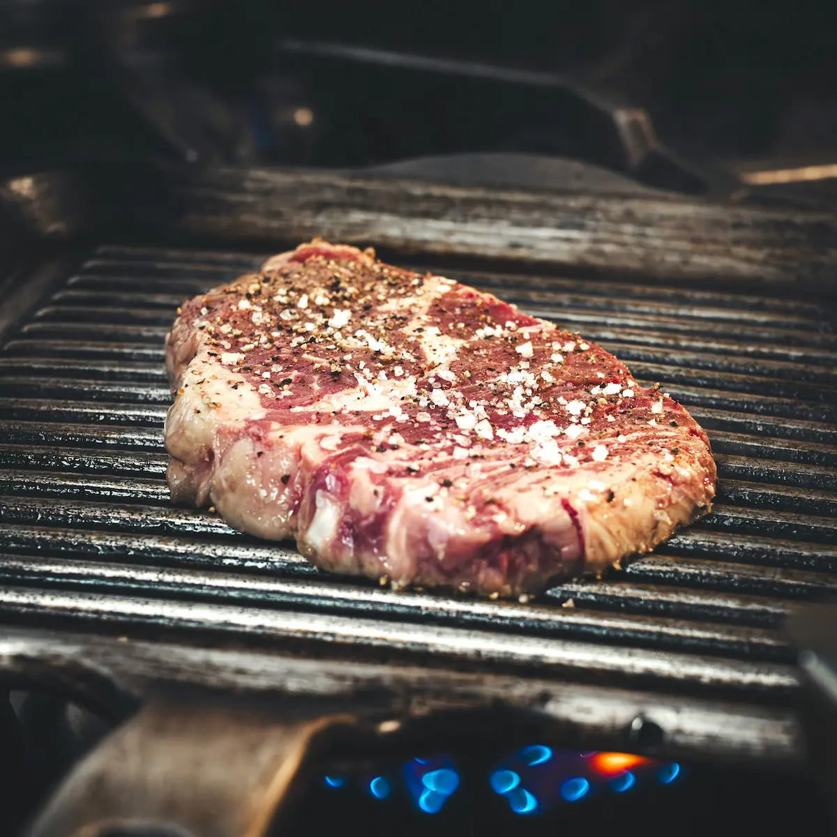 Primer plano de un grueso bistec sazonado cocinándose sobre una parrilla.