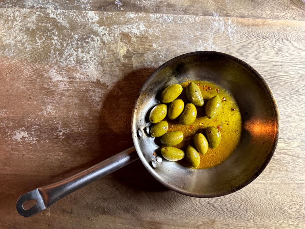 Sartén metálica con aceitunas verdes en aceite de oliva.