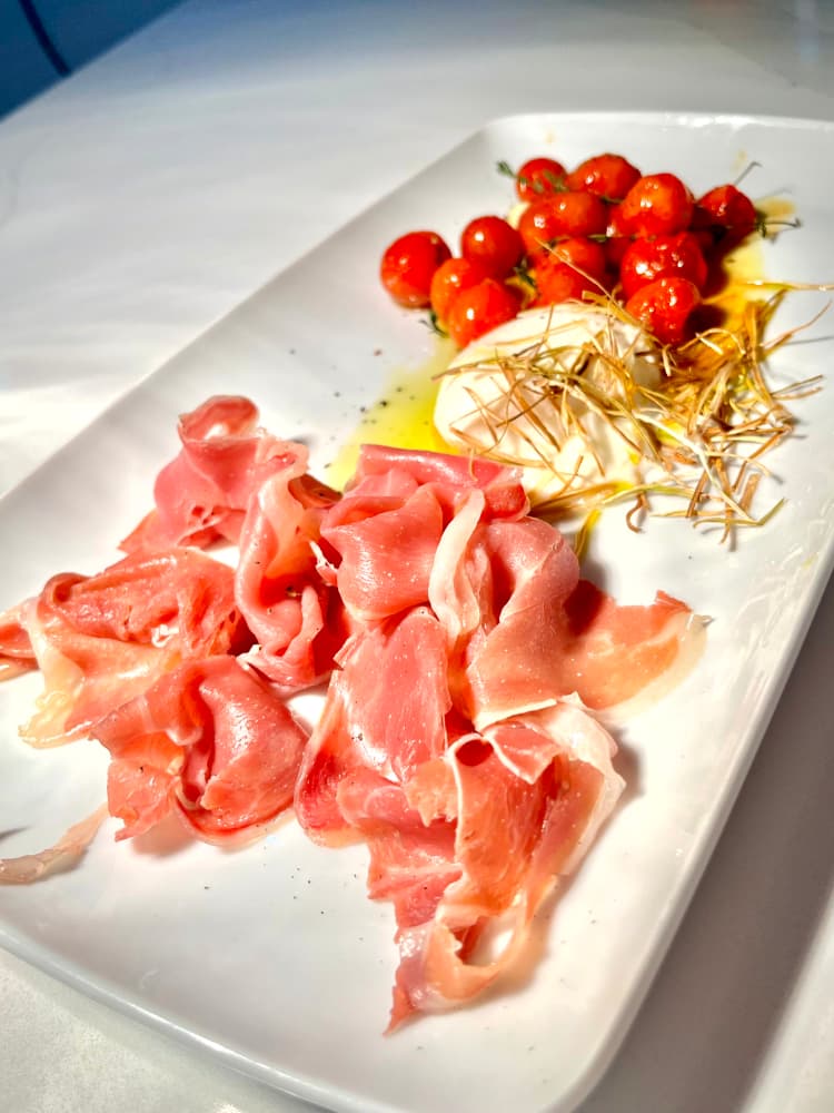 Plato con lonchas de jamón serrano, tomates cherry y crujientes de cebolla.