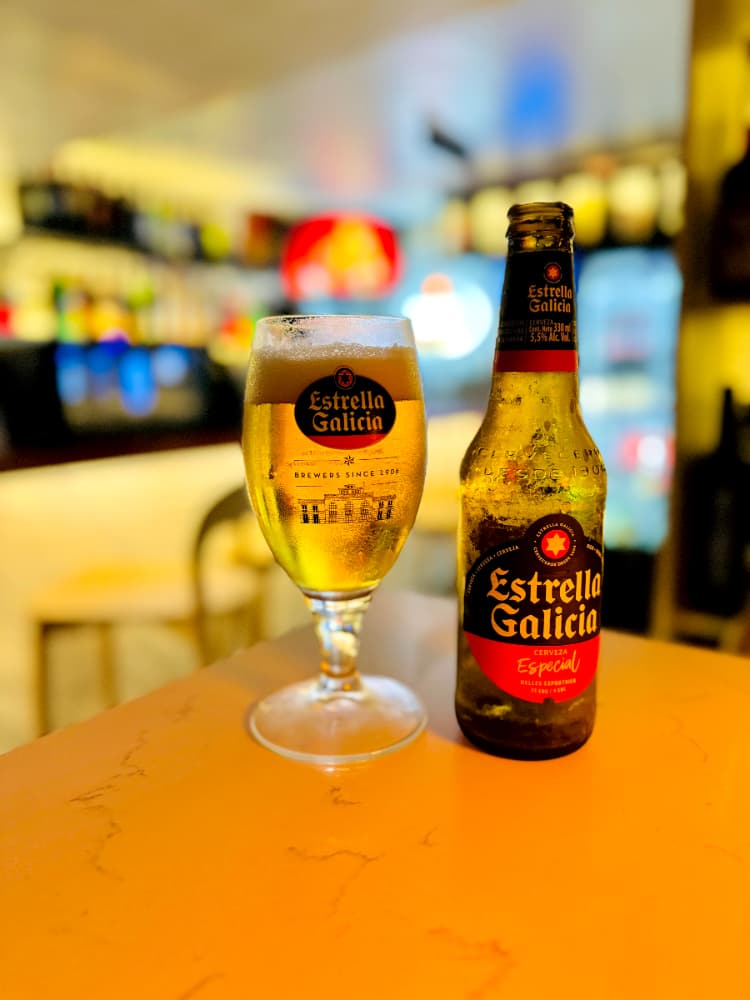 Cerveza Estrella Galicia en vaso y botella sobre una mesa en bar.