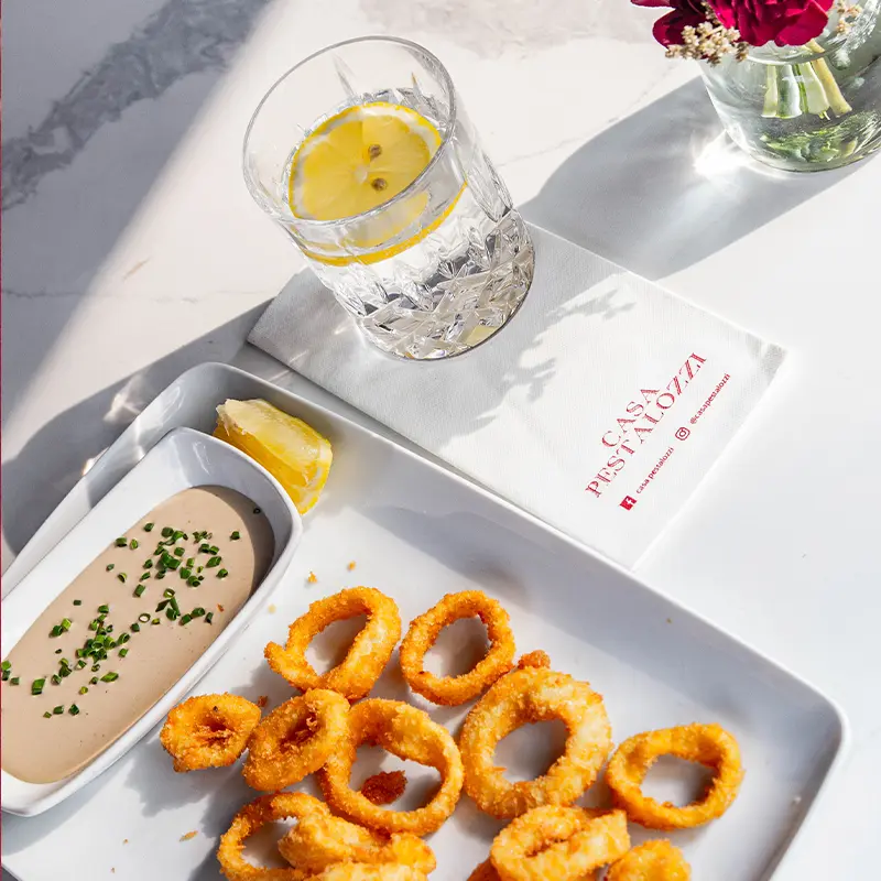 Palto con aros de cebolla y salsa, acompañado de una bebida fresca con una rodaja de limón.