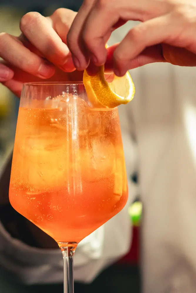 Cóctel naranja con rodaja de cítrico siendo preparado.