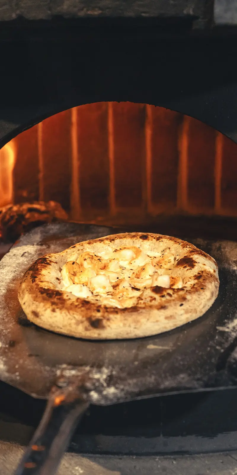 Pizza artesanal dorándose dentro de un horno de leña encendido, mostrando su corteza crujiente y queso fundido.