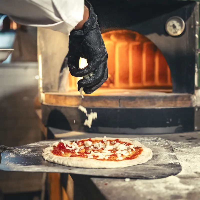 Chef agregando queso a una pizza artesanal justo antes de introducirla en un horno de leña tradicional
