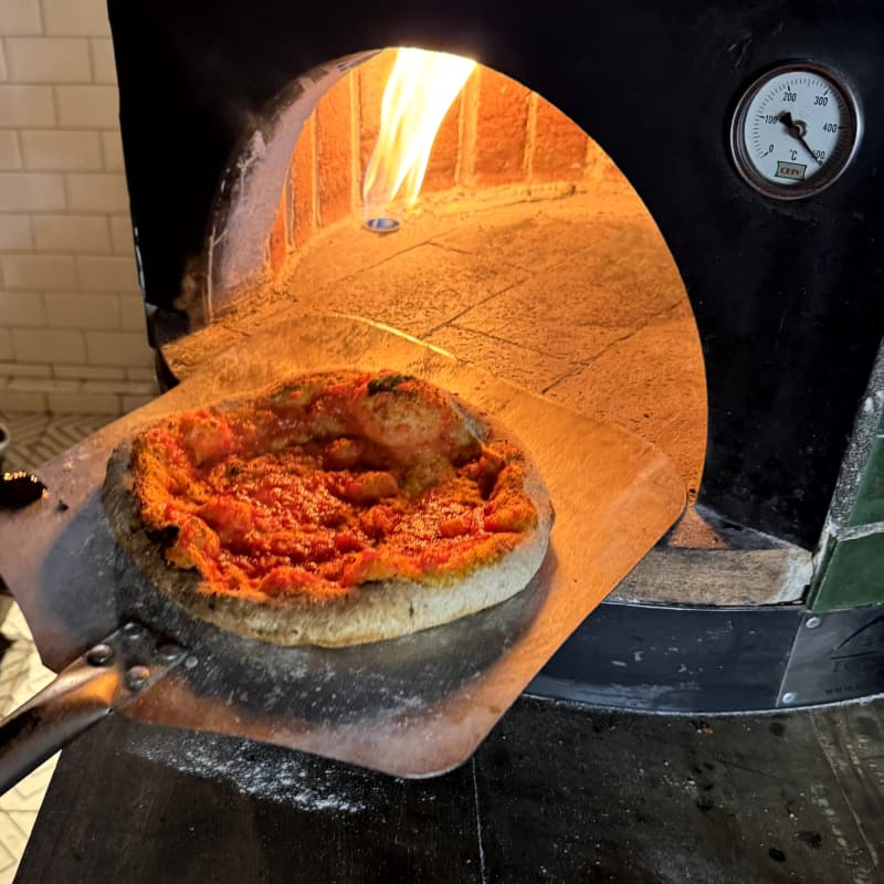 Pizza de pepperoni dentro de un horno de ladrillo, colocada sobre una pala de madera mientras se hornea.